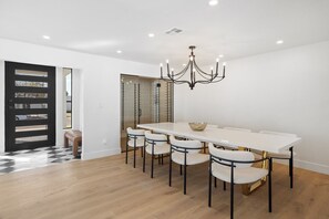 Ein Essbereich mit einem langen wei ßen Tisch, sechs Stühlen, einer Chandelier und einer Bank.