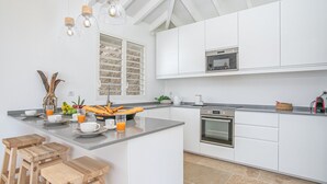 Een moderne keuken met witte kasten, een centraal kookeiland met barkrukken, een magnetron en een inbouwoven.