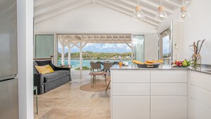Een moderne keuken met uitzicht op zee, een zithoek met een bank en stoelen, en een keukeneiland met fruit en keukengerei.