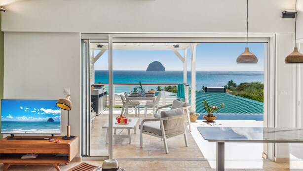 Un salon moderne doté d’un grand téléviseur, d’un coin repas offrant une vue sur l’océan et d’un balcon avec vue sur la mer.