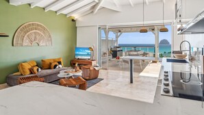 Un salon moderne comprenant un canapé, une table basse et un téléviseur, donnant sur un balcon avec vue sur la mer.