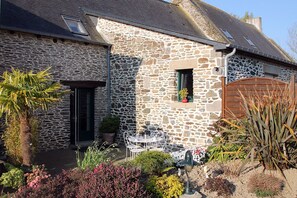 Ein Steinhaus mit kleiner Terrasse, einer Tür und einem Fenster mit Pflanze.