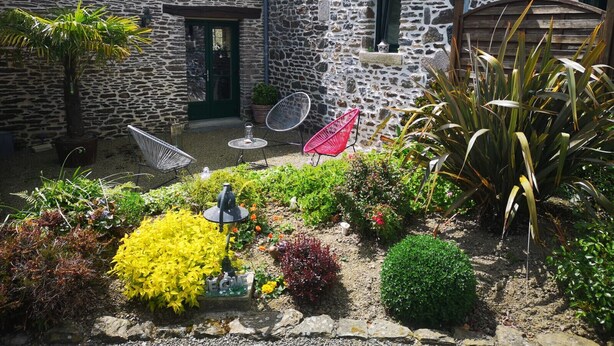 Un edificio de piedra con un pequeño patio, mobiliario exterior y diversas plantas.