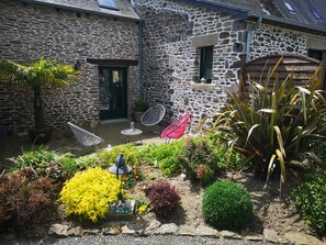 A stone building with a small patio area, outdoor seating, and various plants. - Le Petit Porcon (Saint-Méloir-des-Ondes)