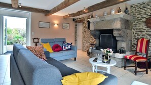 Una sala de estar con chimenea de piedra, un sofá gris con cojines coloridos y una silla de madera.
