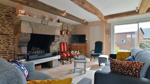 Una sala de estar acogedora con chimenea de piedra, vigas de madera, televisor de pantalla plana y asientos cómodos.