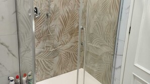 A bathroom with a glass shower enclosure, marble walls, and a white countertop. - Bnb Massaua (Torino)