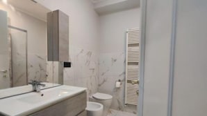 A modern bathroom with a large mirror, a vanity with a sink, a toilet, and a shower area. - Bnb Massaua (Torino)