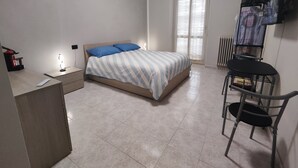 A bedroom with a bed, a desk, a chair, a radiator, and a window with blinds. - Bnb Massaua (Torino)