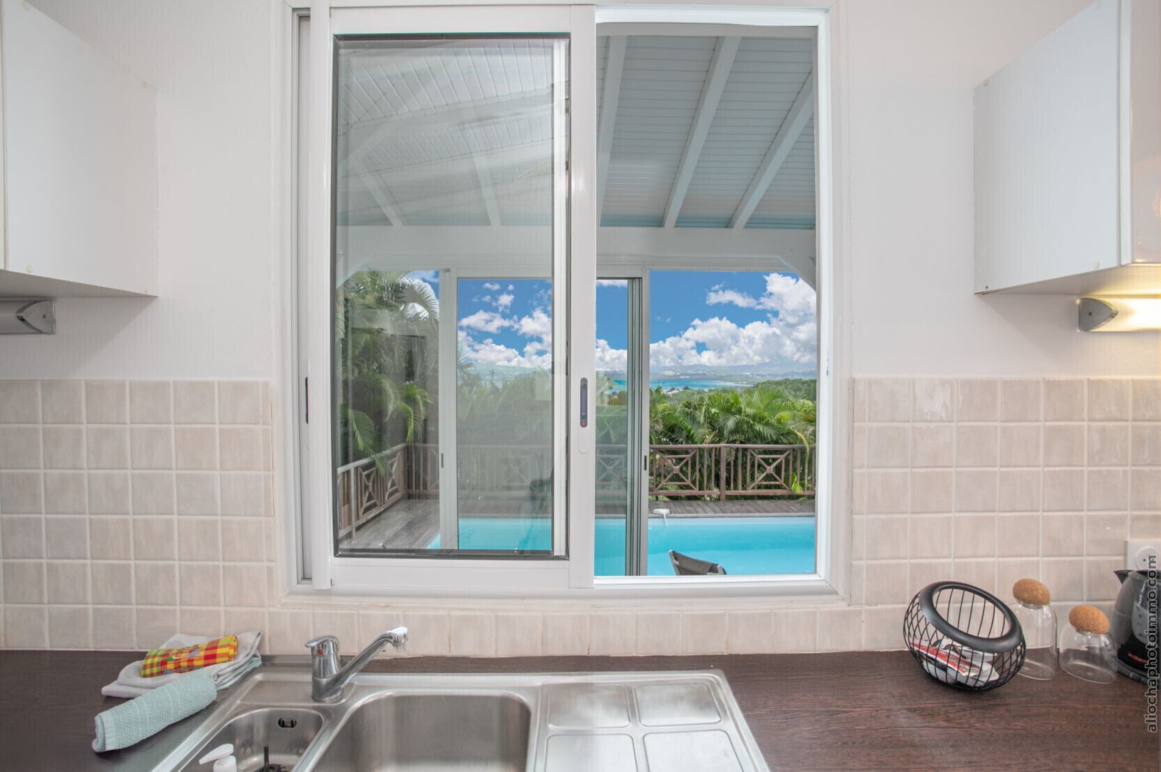 A kitchen with a large sliding glass door leading to a pool area, a stainless steel sink, and a wooden countertop.