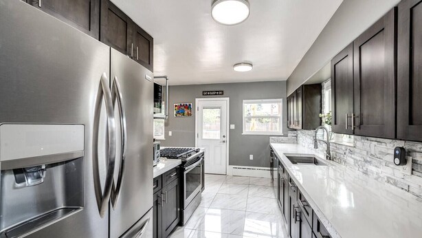 A modern kitchen with stainless steel appliances, dark cabinetry, and a marble countertop. - Relax & Recharge – Spacious Wheatridge Stay w/ Backyard Fun (Wheat Ridge)