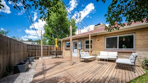A wooden deck with outdoor furniture, a fenced area, and a building with large windows. - Relax & Recharge – Spacious Wheatridge Stay w/ Backyard Fun (Wheat Ridge)