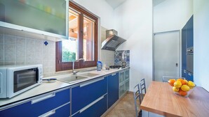 Une cuisine avec des meubles bleus, un four à micro-ondes, un évier et une table en bois sur laquelle se trouve un saladier rempli de fruits.