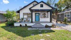 A two-story house with a blue door, a front porch with a bench, and a number 1505 displayed on the front steps.
