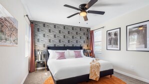 A bedroom with a bed, a ceiling fan, patterned wallpaper, and framed pictures on the walls.