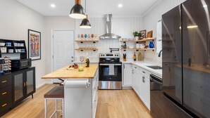 A modern kitchen with white cabinetry, a wooden island, stainless steel appliances, and pendant lighting.