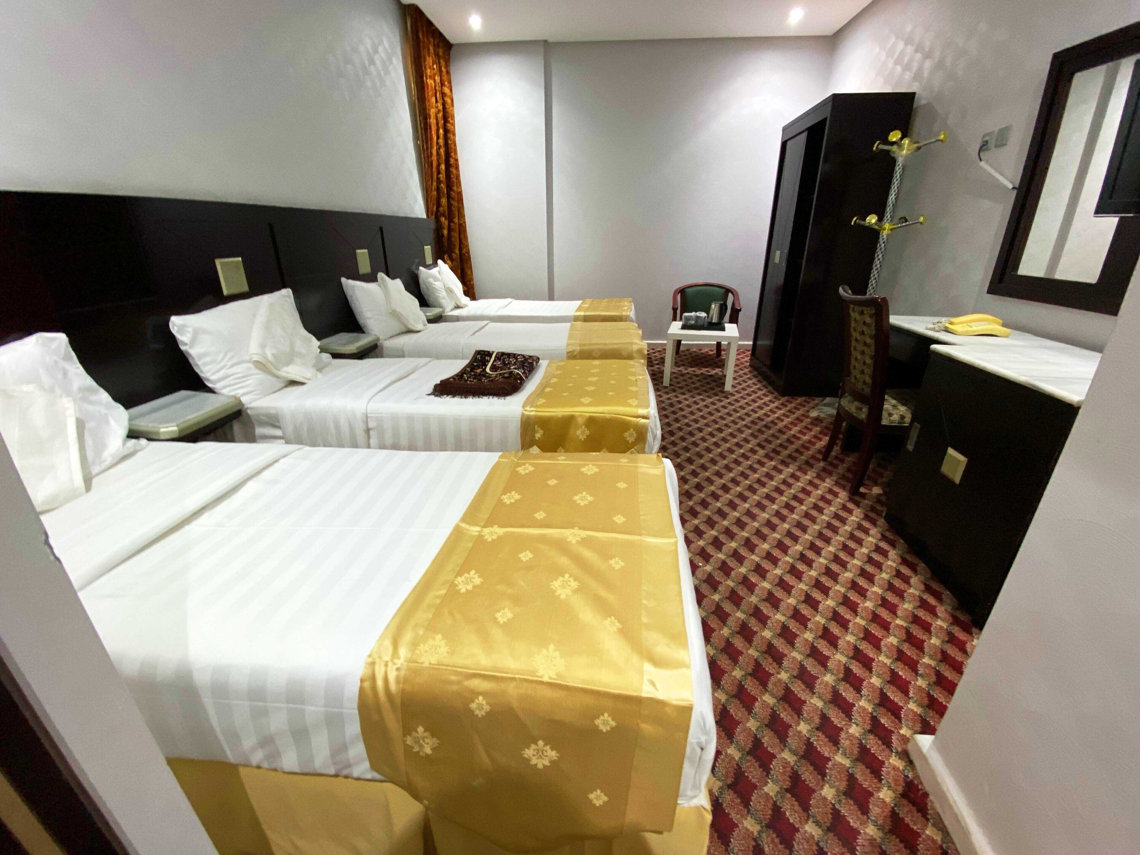 A hotel room with two beds, a small table, a chair, a desk, and a mirror.
