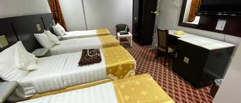 A hotel room with four beds, a desk, a chair, a TV, and a minibar.