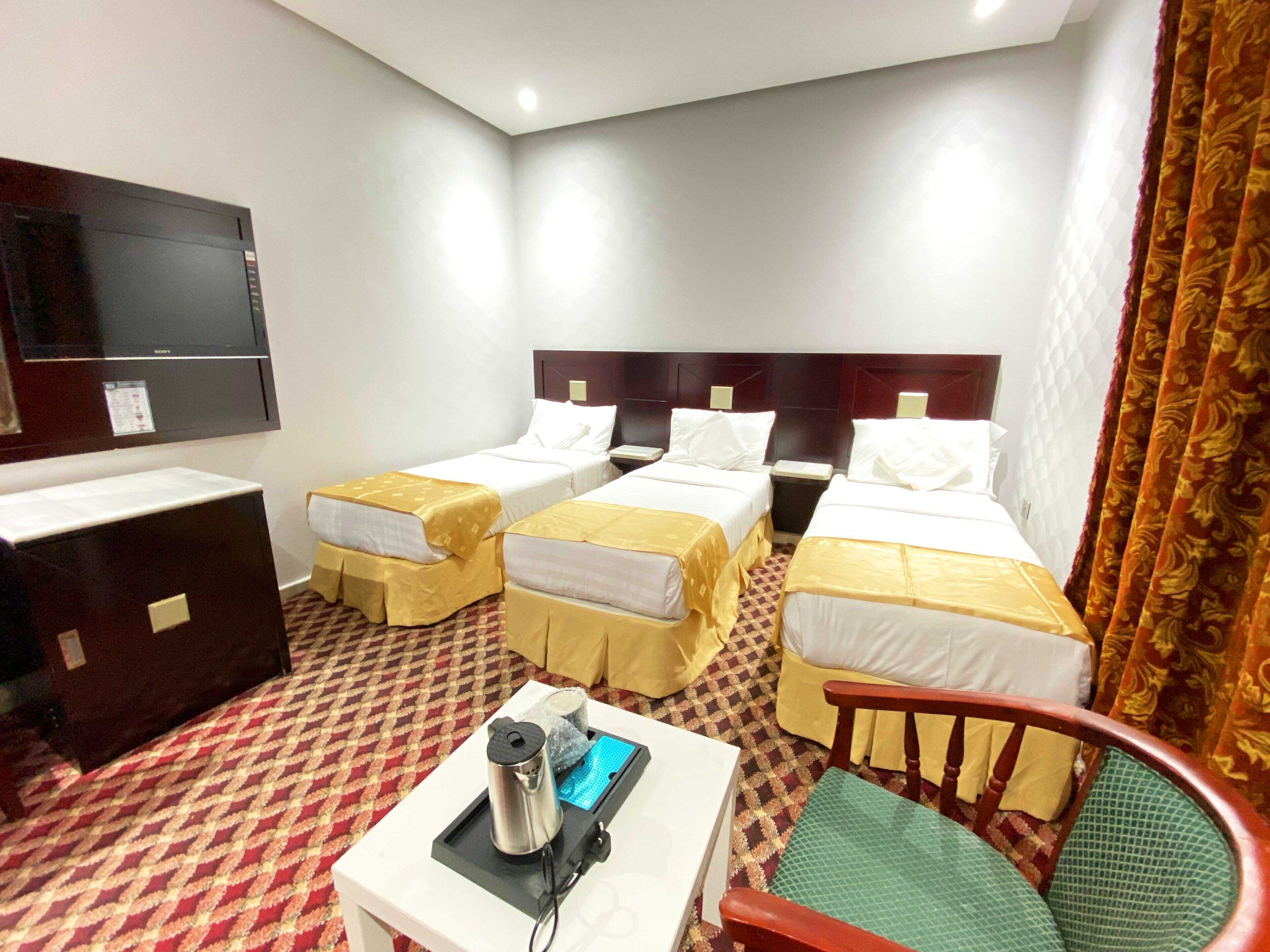 A hotel room with two single beds, a desk, a chair, a TV, and a small table with a kettle and a power strip.