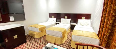 A hotel room with two single beds, a desk, a chair, a TV, and a small table with a kettle and a power strip.