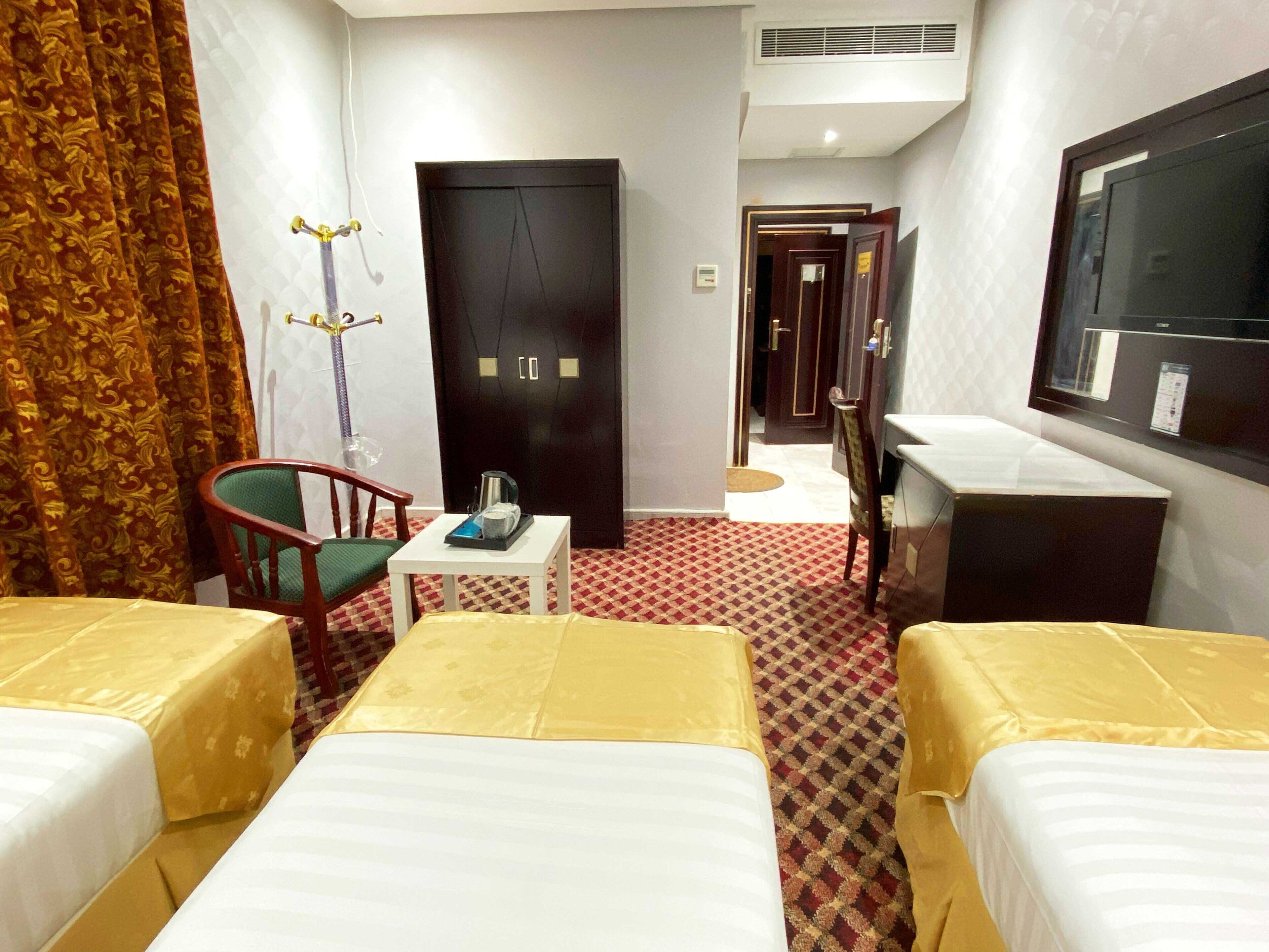 A hotel room with two beds, a desk, a chair, a wardrobe, and a television.