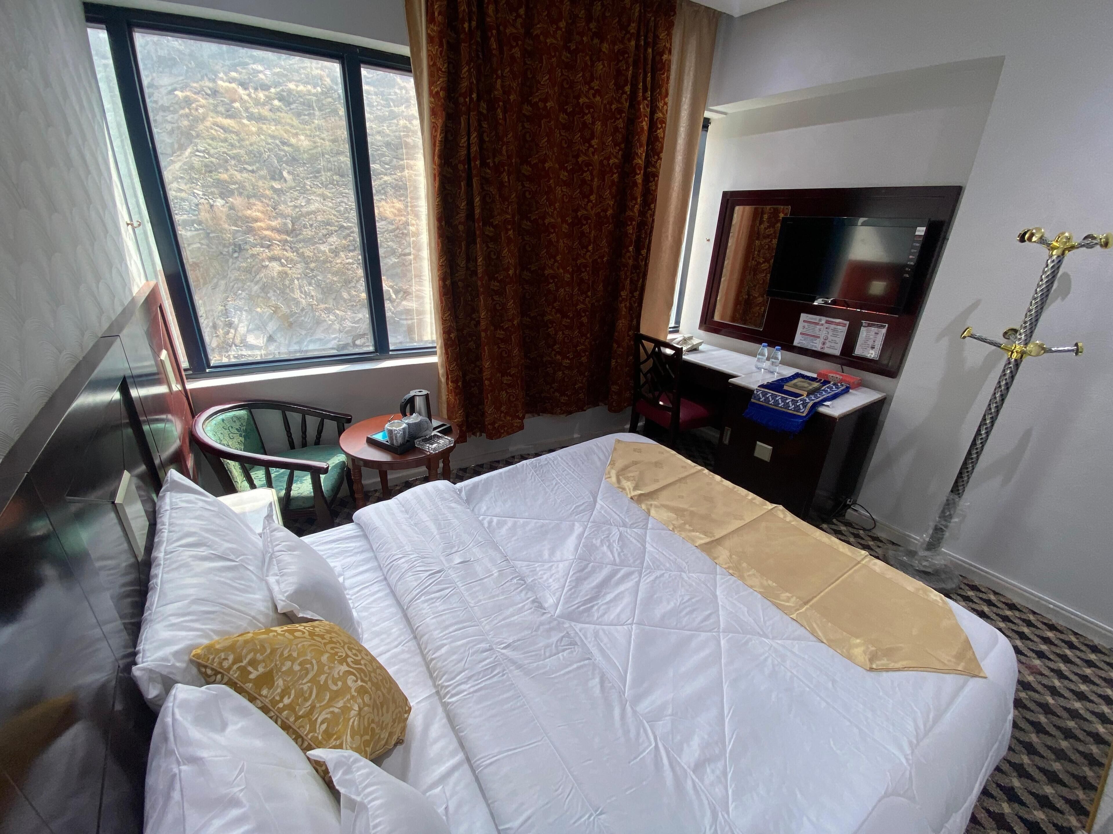 Habitación de hotel con cama, escritorio, silla, mesita, ventana con cortinas y zona de ducha.