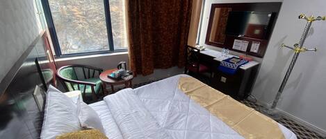 Habitación de hotel con cama, escritorio, silla, mesita, ventana con cortinas y zona de ducha.