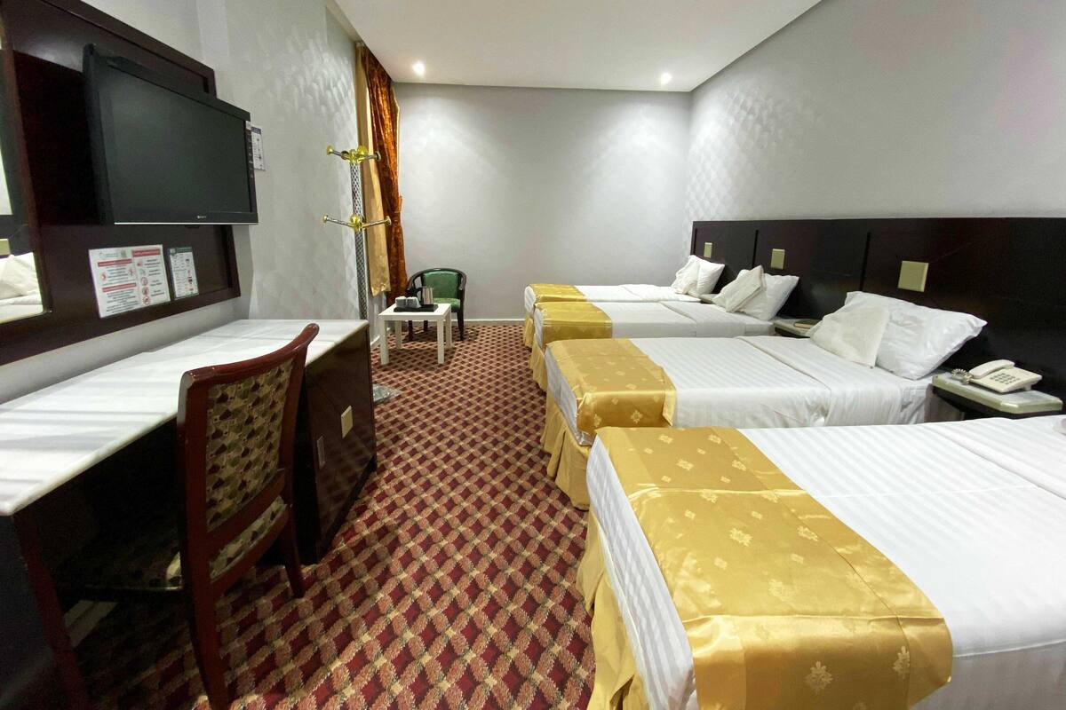 Habitación de hotel con dos camas, un escritorio, una silla, un televisor y una mesita con otra silla.