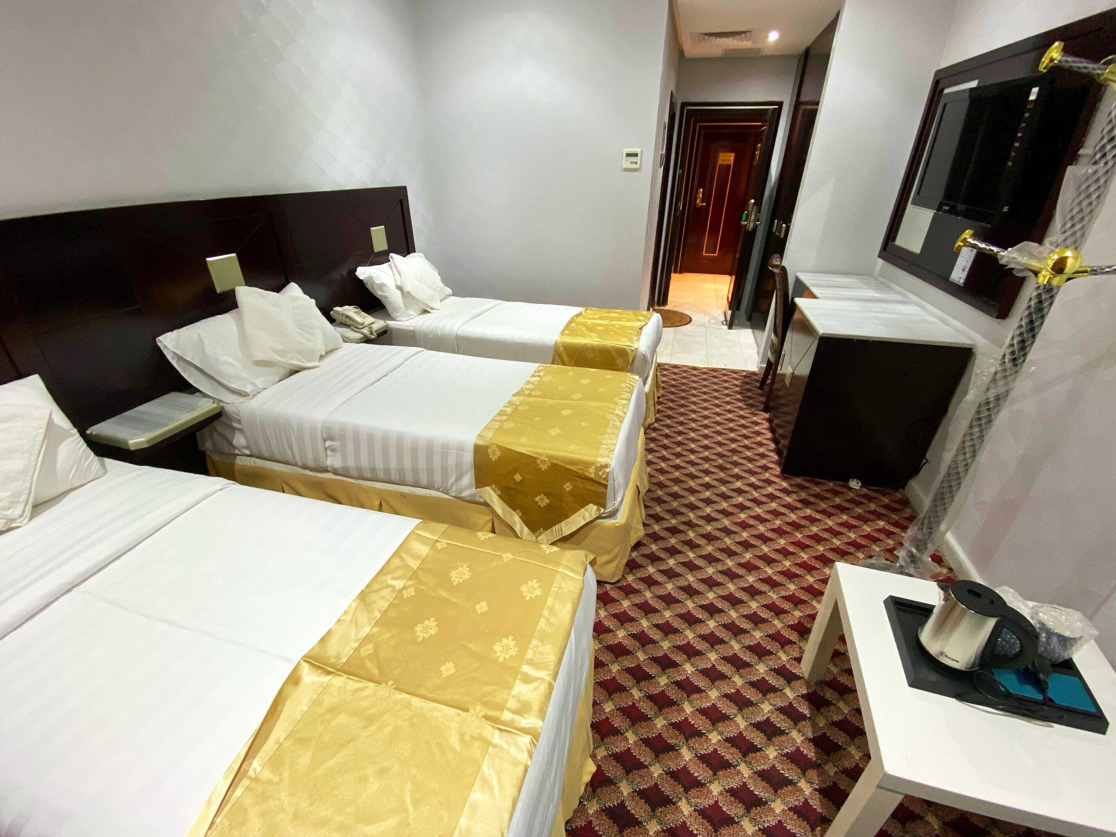 A hotel room with three beds, a desk, a chair, a mirror, and a television.