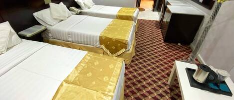 A hotel room with three beds, a desk, a chair, a mirror, and a television.