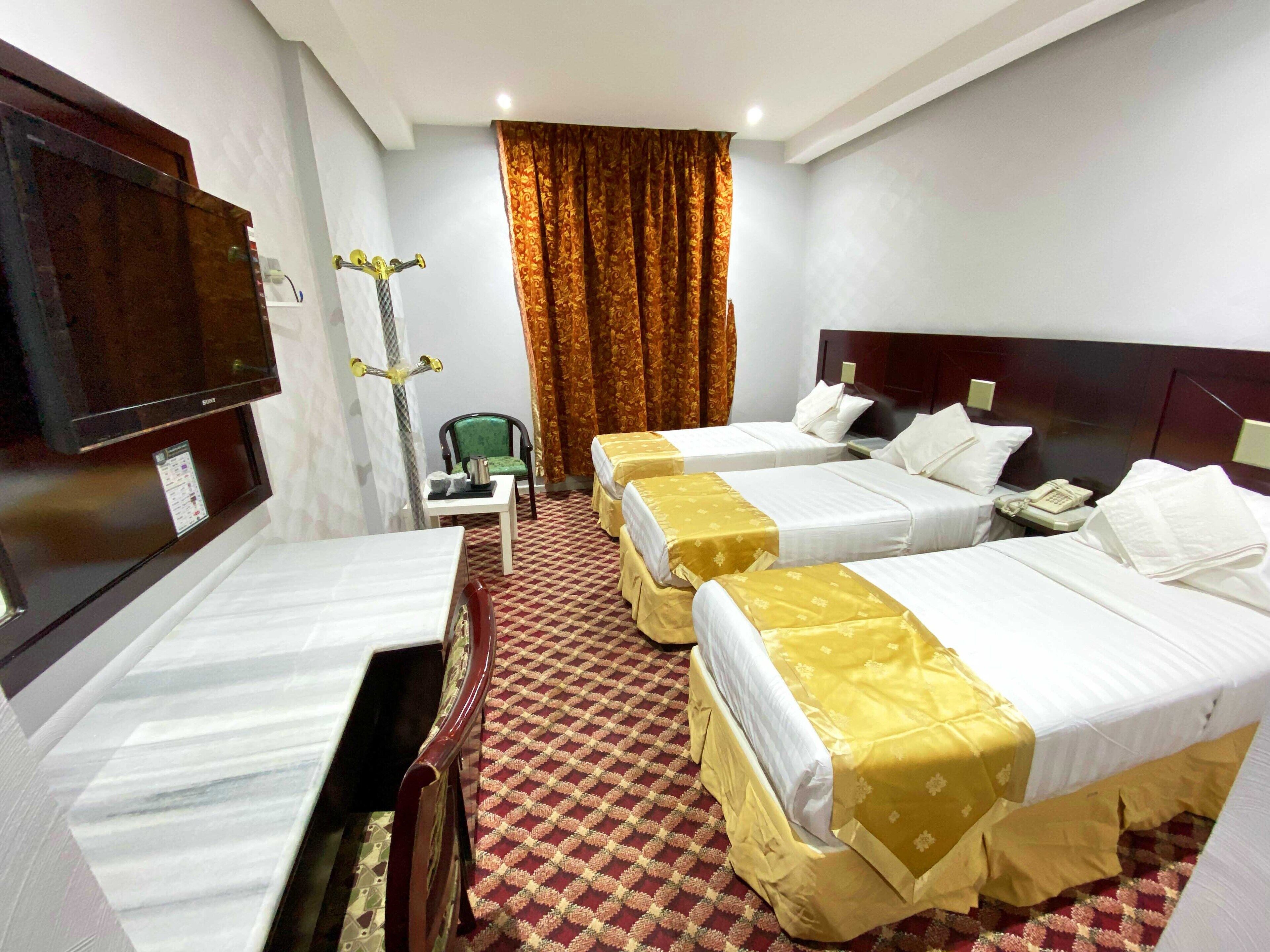 Une chambre d’hôtel avec trois lits, un bureau, une chaise, une télévision et un téléphone.