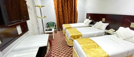 Una camera d'albergo con tre letti, una scrivania, una sedia, una televisione e un telefono.