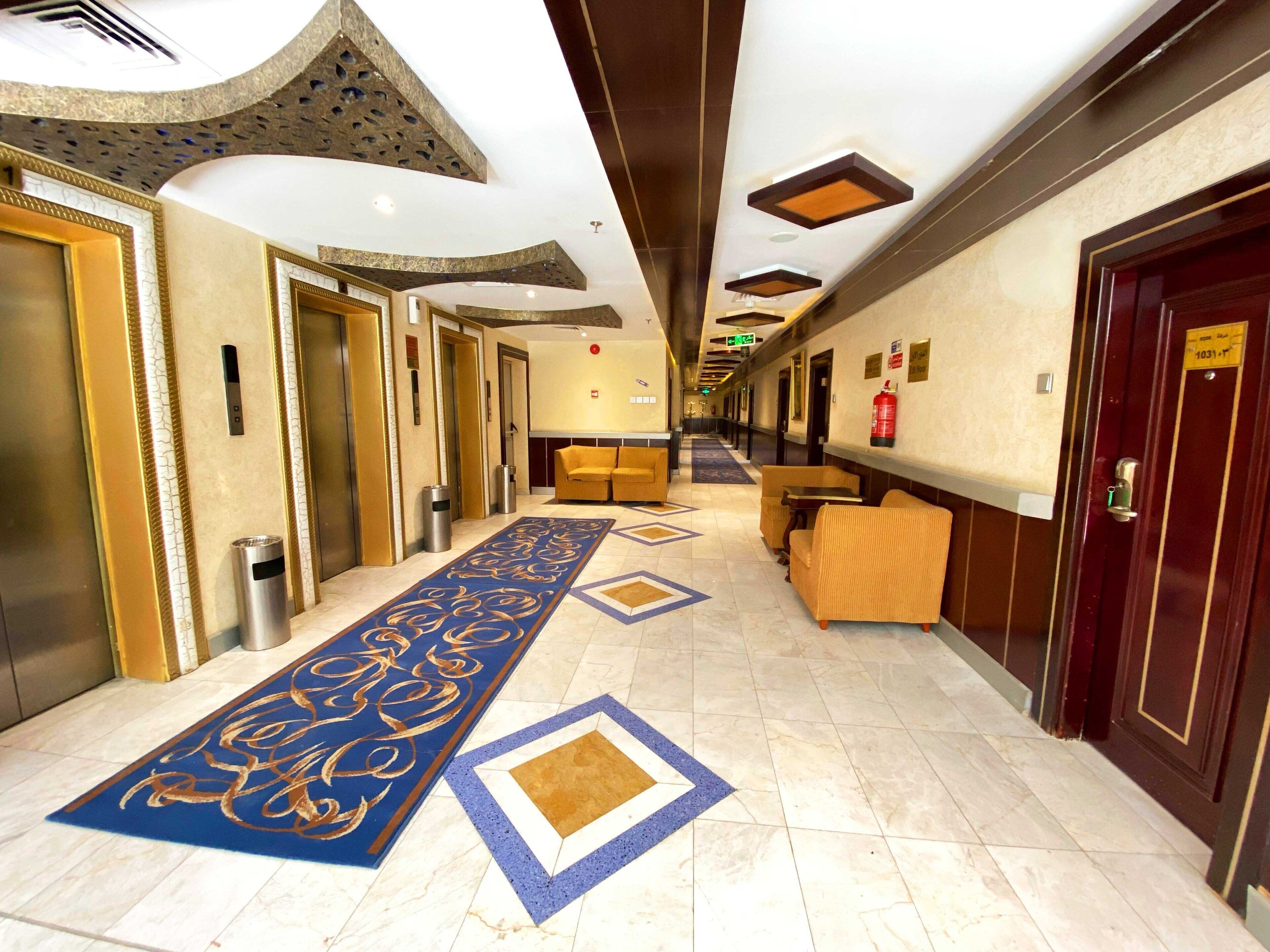 Un pasillo de hotel con alfombra azul, un mostrador de recepción y un extintor en la pared.