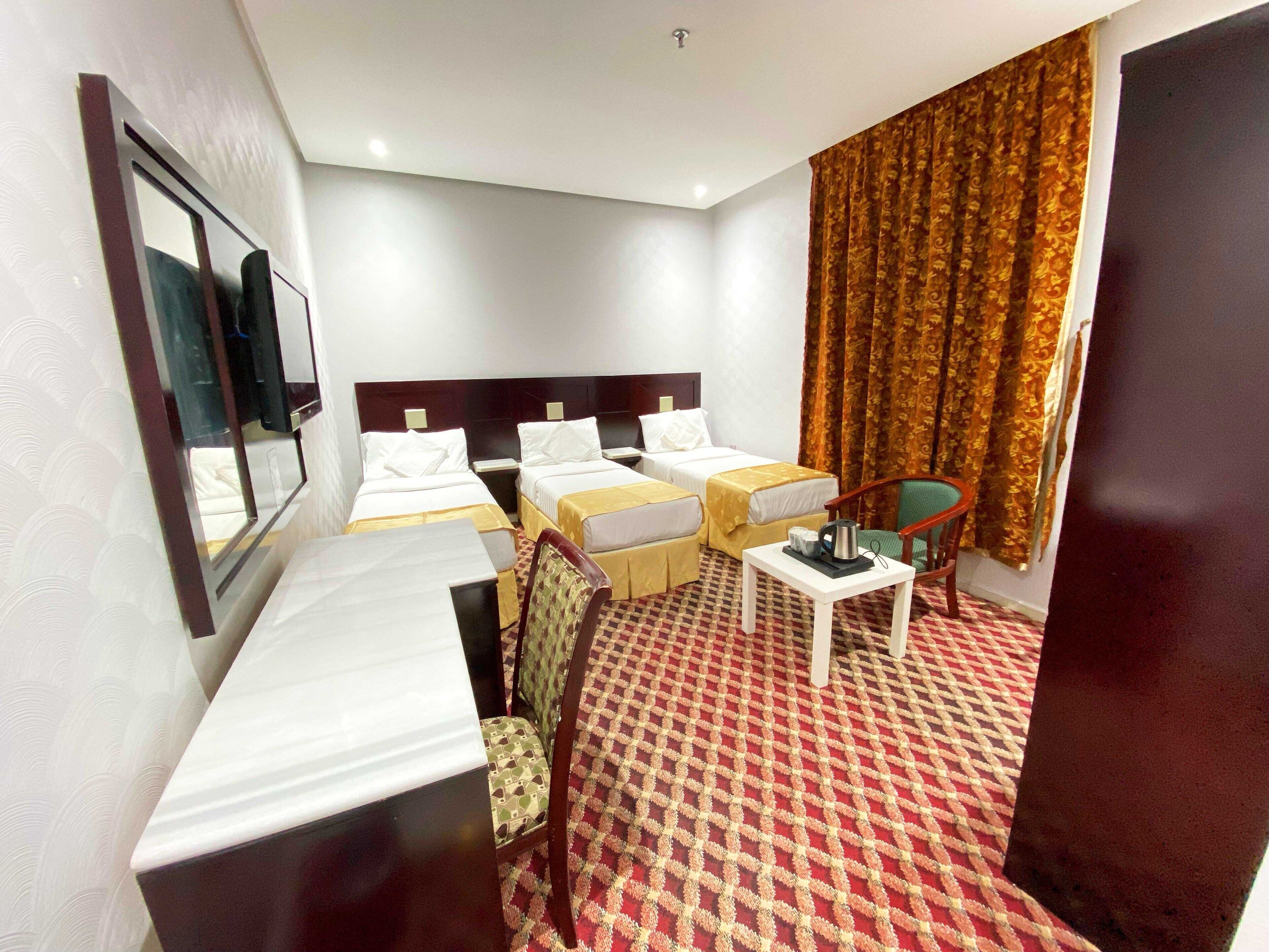 A hotel room with two single beds, a small table, a chair, and a desk.