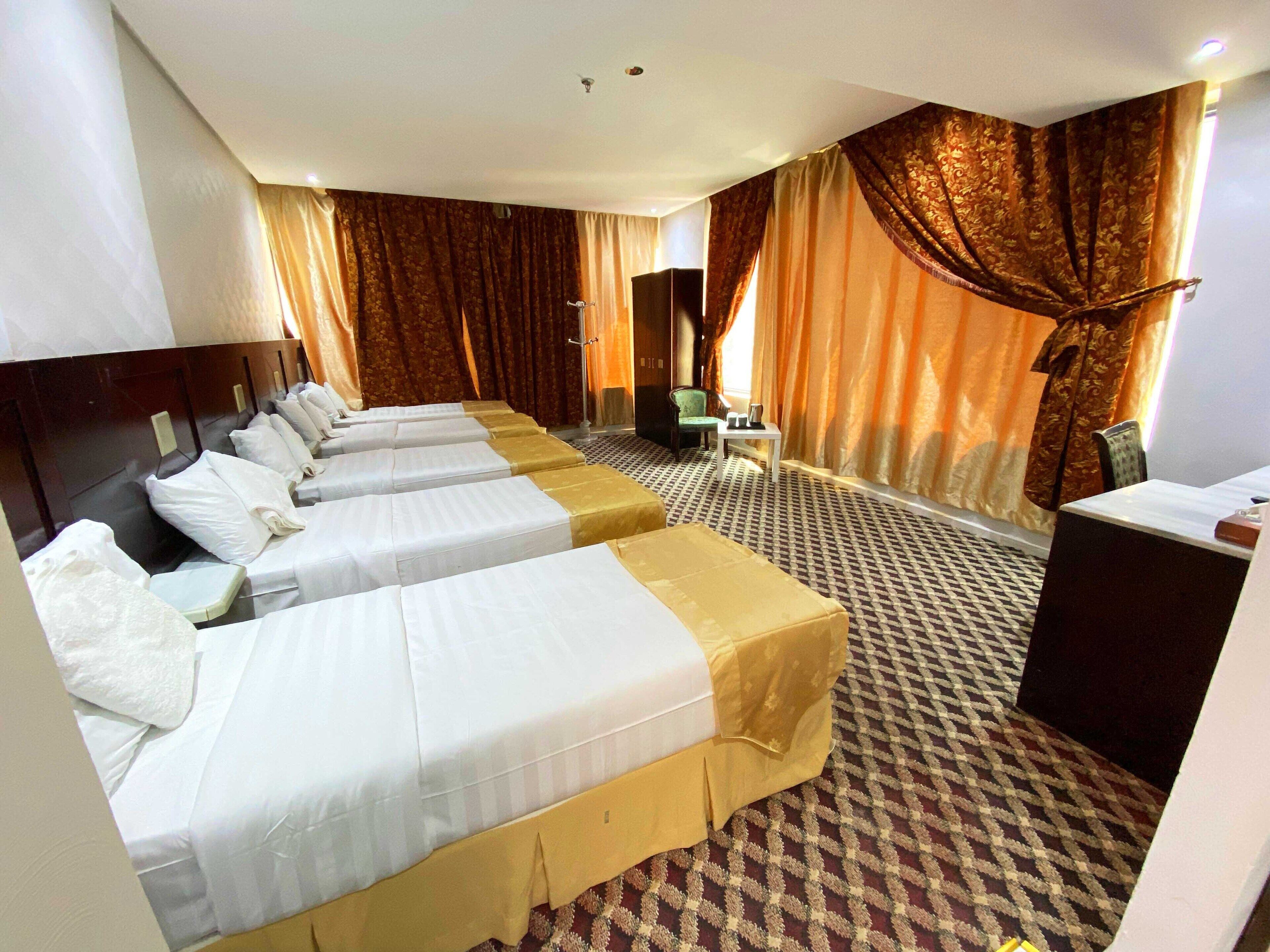 A hotel room with four single beds, a desk, a chair, and a small table.