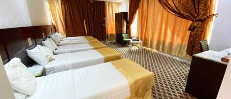 A hotel room with four single beds, a desk, a chair, and a small table.