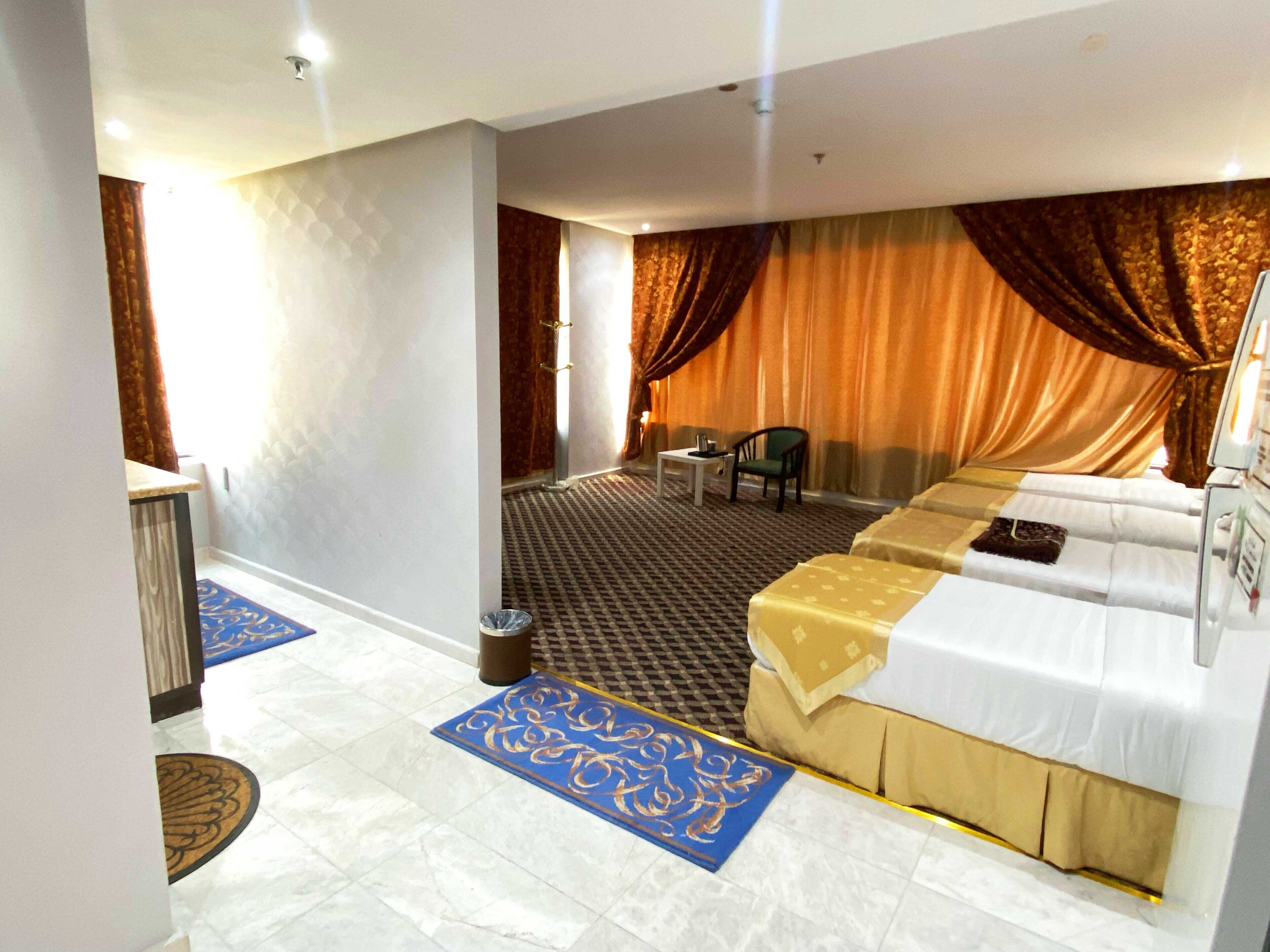 Ein Hotelzimmer mit einem großen Bett, einem Schreibtisch und einem Sessel. Es gibt ein Fenster mit Vorhängen und einen Teppichboden.