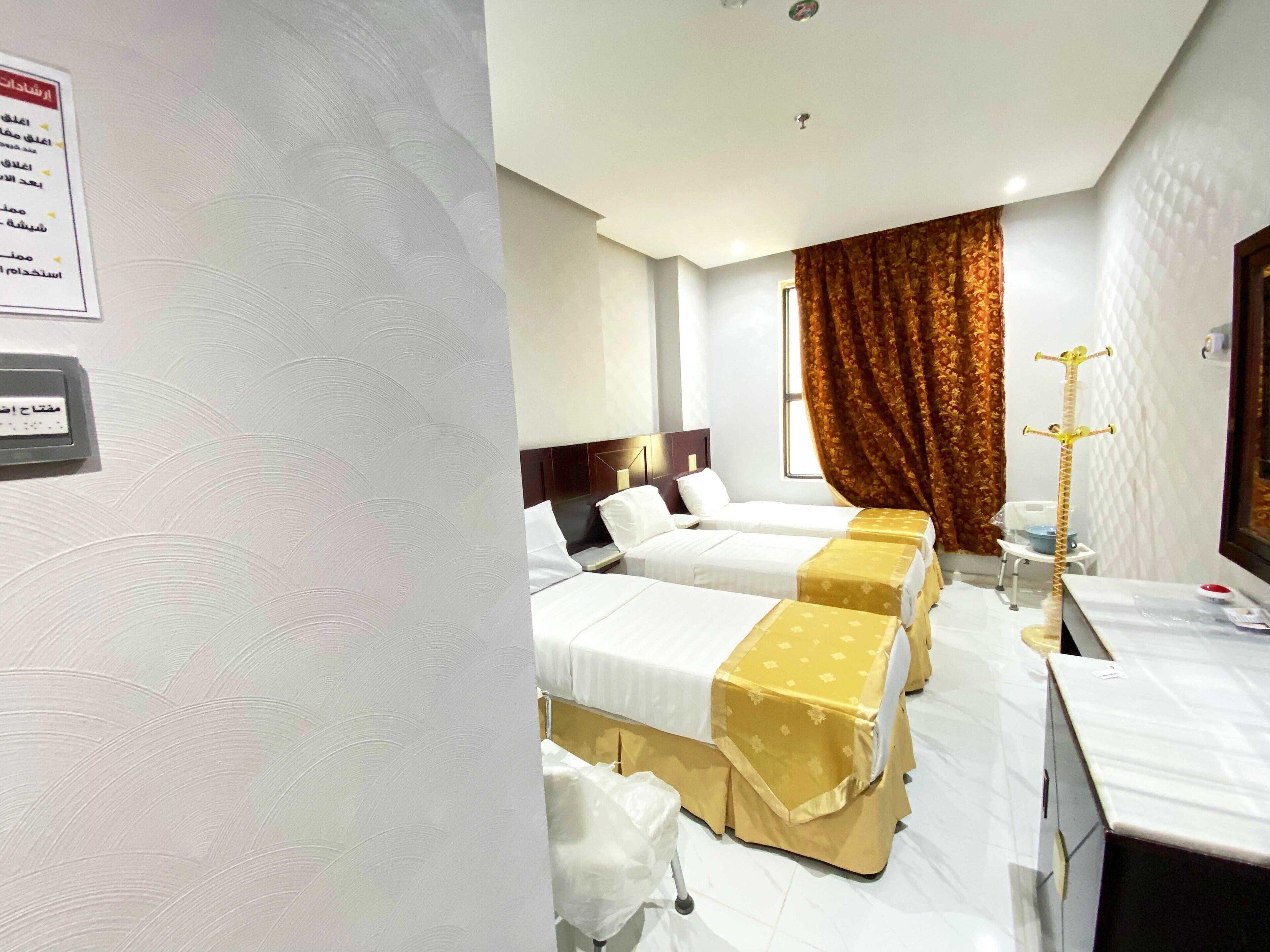 A hotel room with two beds, a desk, a chair, a small table, and a decorative plant.