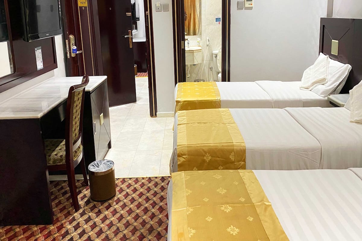 Habitación de hotel con cama, mesita de noche y escritorio con silla. Hay un bote de basura y una alfombra estampada en el suelo.