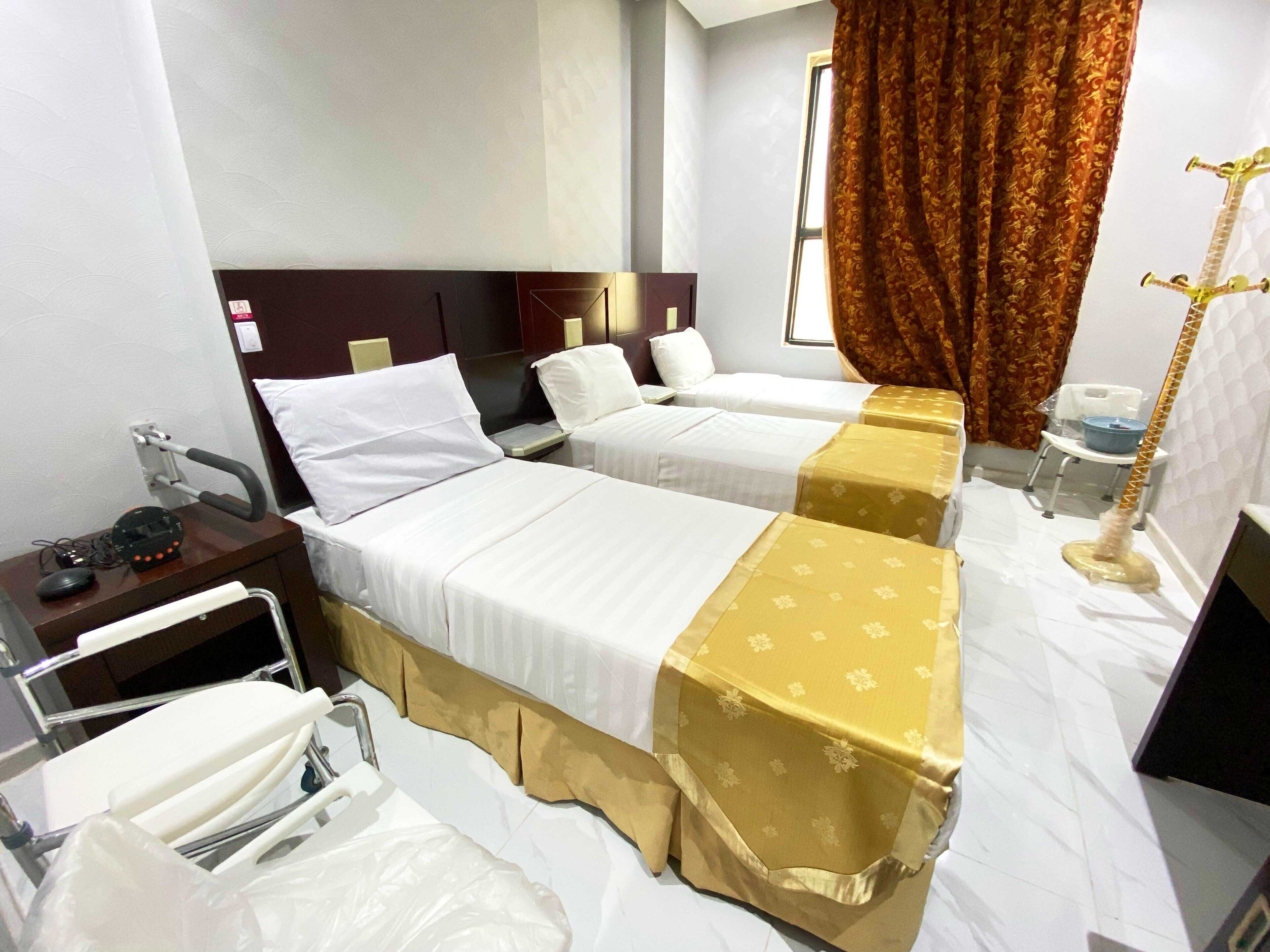 A hotel room with two beds, a bedside table, a chair, a desk, a telephone, and a window with curtains.