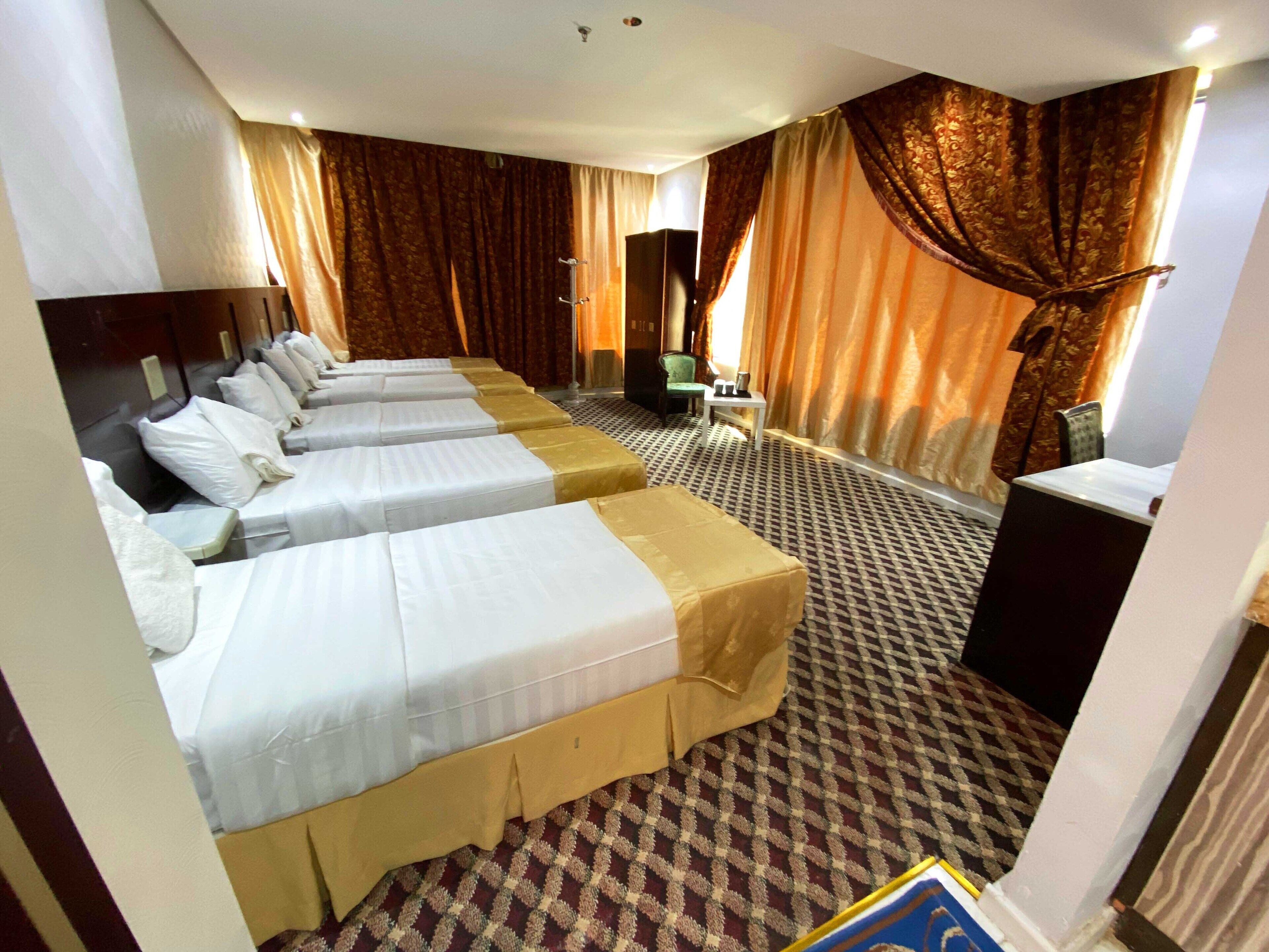 A hotel room with four single beds, a small desk, a chair, and a television.