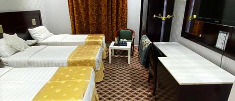 Una habitación de hotel con tres camas, un escritorio, una silla, un televisor y una alfombra estampada.