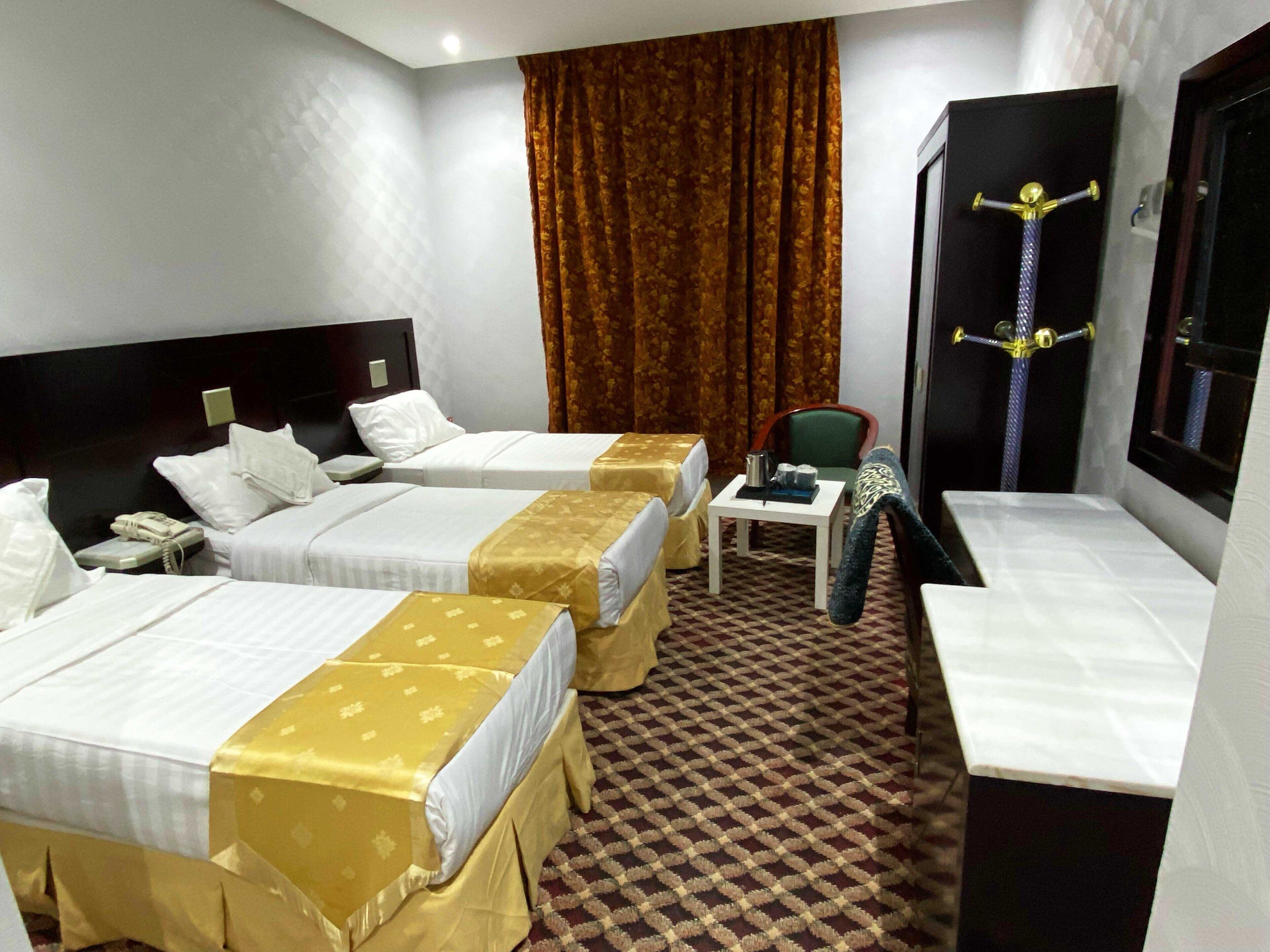 A hotel room with two beds, a small table, a chair, a desk, and a window with curtains.