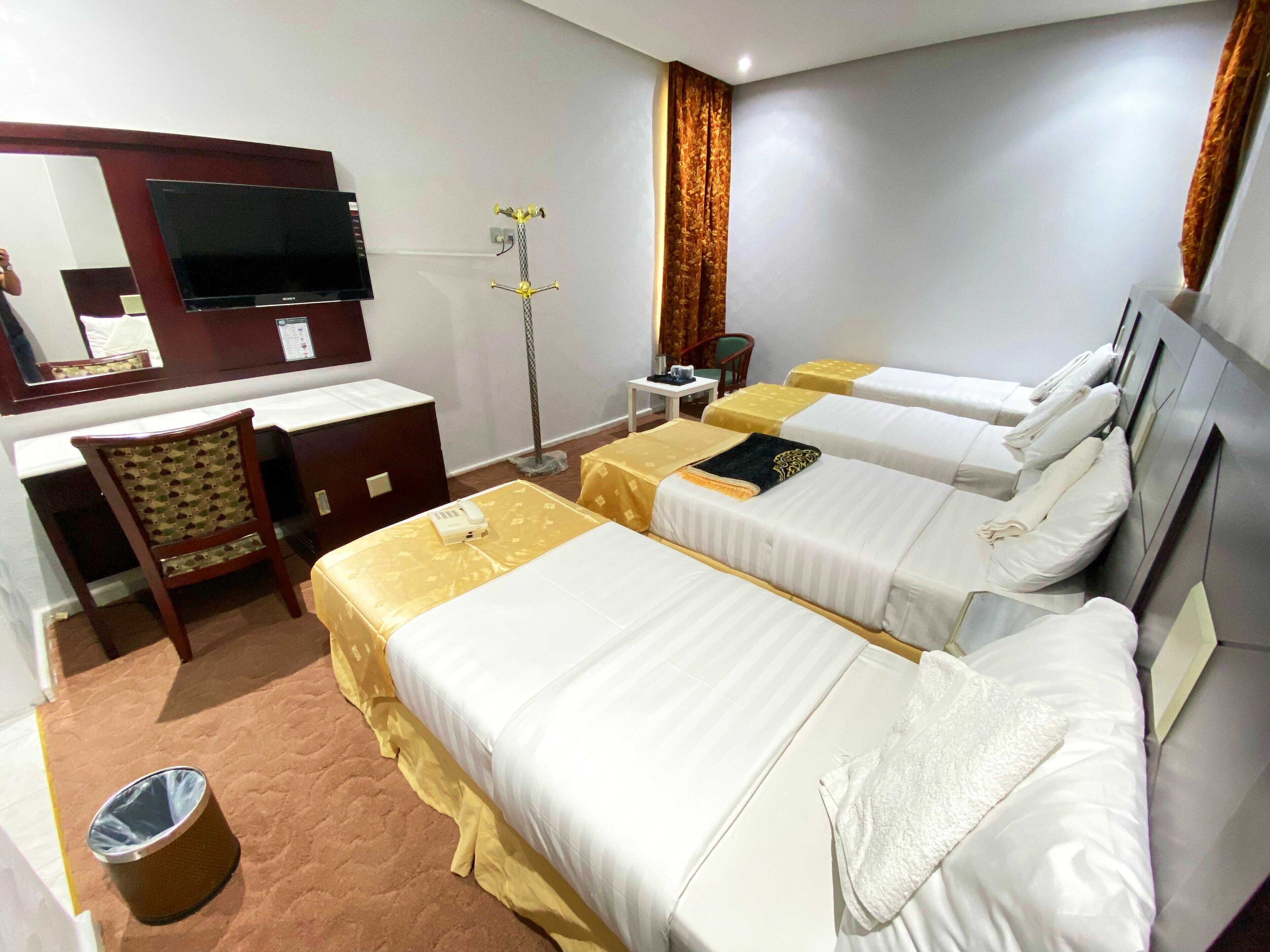 A hotel room with two single beds, a desk with a chair, a TV, a telephone, and a trash bin.