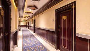 A hotel hallway with a blue carpet, dark wooden doors, and a light-colored wall. - alroh alhora hotel (Makkah)