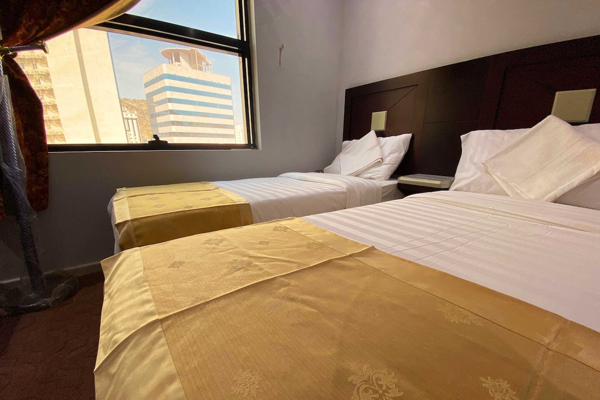 Habitación de hotel con dos camas, una con cubrecama amarillo y la otra con cubrecama blanco. Se ve un edificio a través de la ventana.