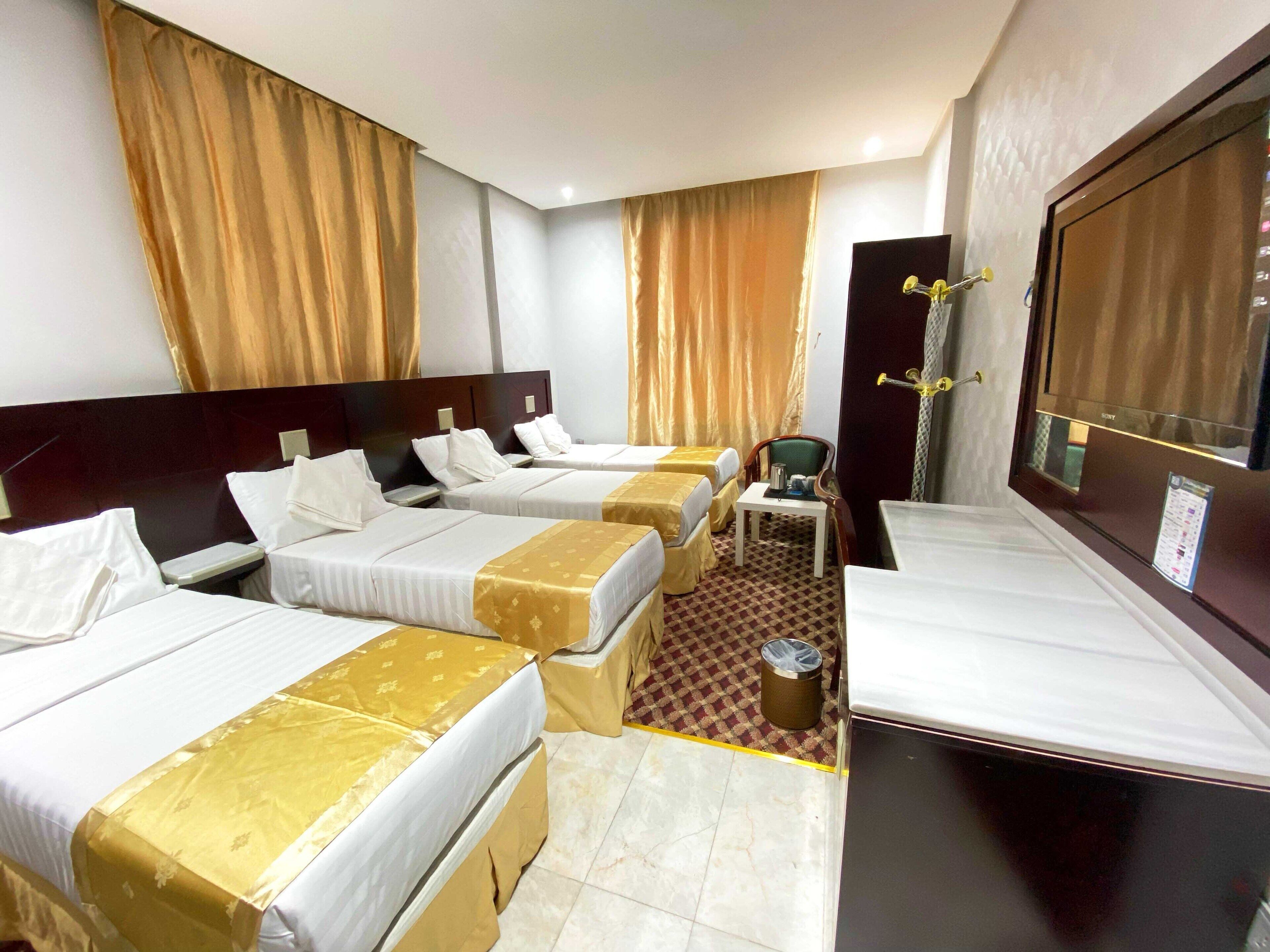 Habitación de hotel con tres camas, una mesita pequeña con una silla y un ventanal grande.
