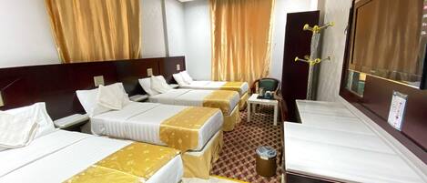 A hotel room with three beds, a small table with a chair, and a large window.