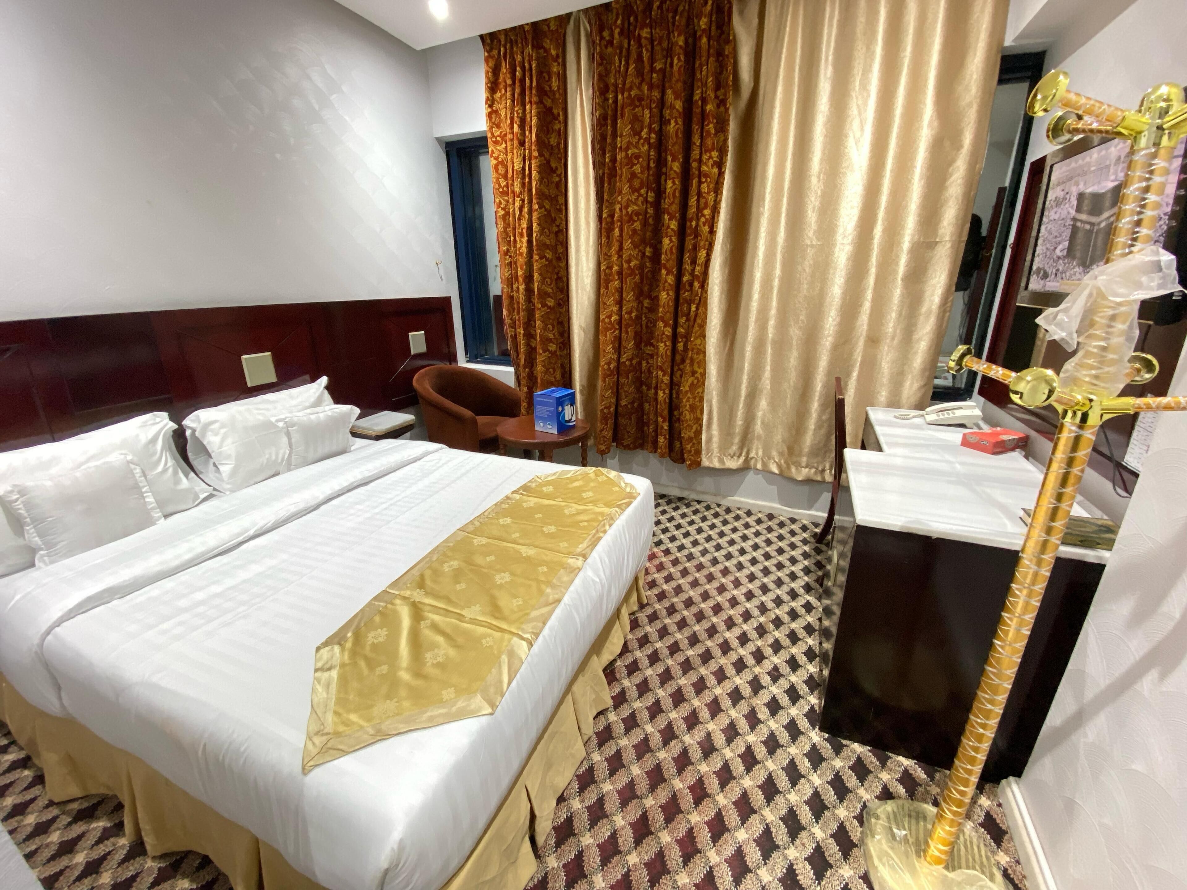A hotel room with a large bed, a chair, a small table, and a mirror.