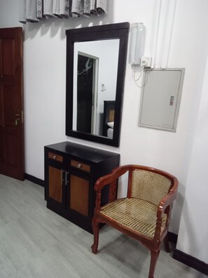 A room with a wardrobe, wicker chair, and large mirror.